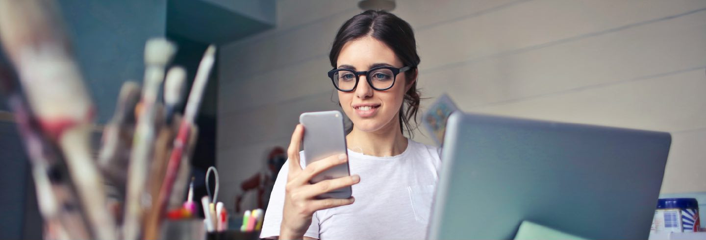 Woman using a mobile device while working at a desktop computer