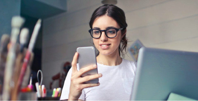 Woman using a mobile device while working at a desktop computer